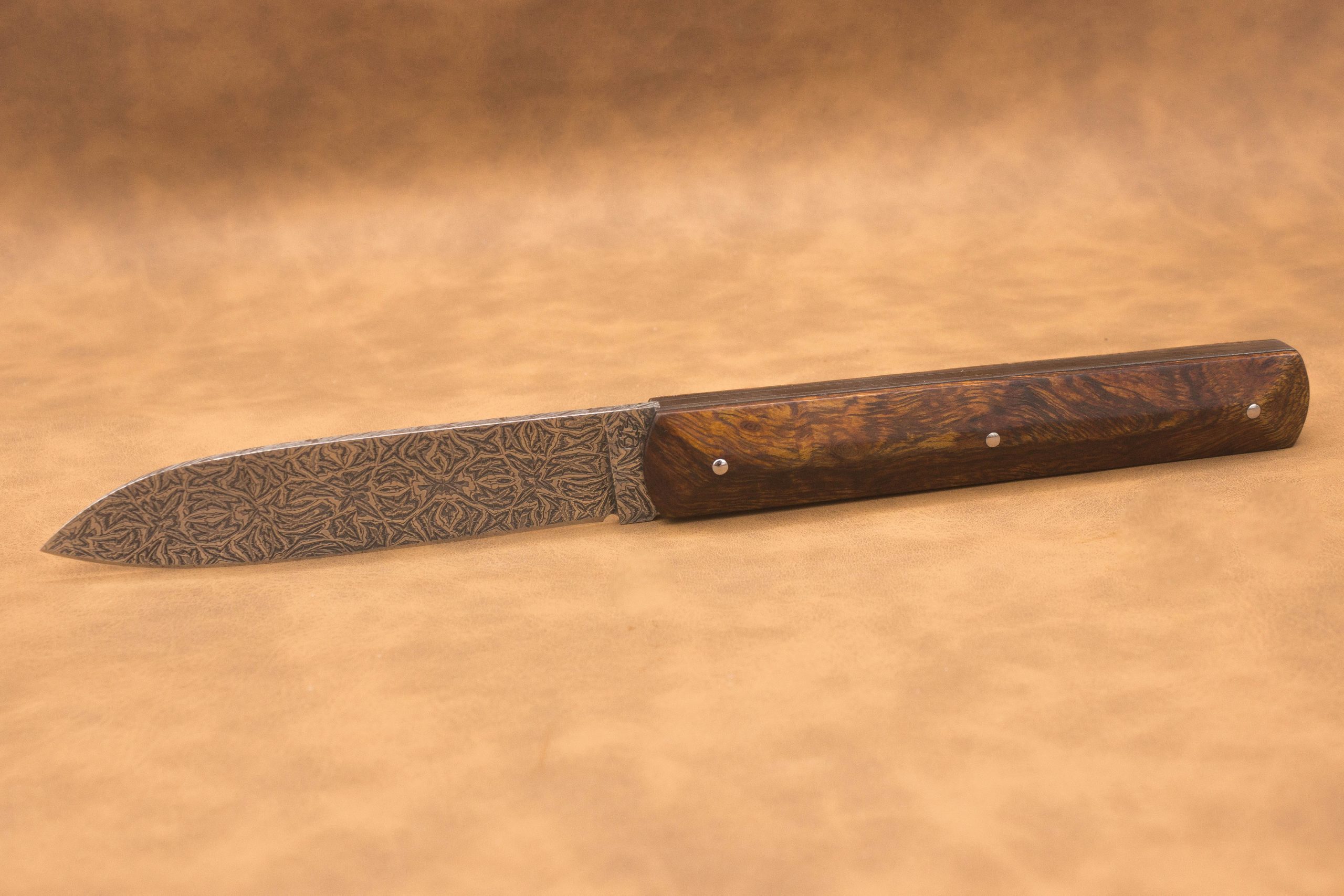 Vue générale : Couteau droit artisanal en damas mosaïque avec manche en bois de fer d'Arizona. Lame : Lame en damas carbone mosaïque forgée artisanalement. Manche : Manche en bois de fer d'Arizona sur couteau artisanal français. Dos : Dos poli d'un couteau à cran forcé fabriqué à la main. Étui : Étui en véritable cuir noir livré avec le couteau artisanal joel alexanian couteau d'art collection damas maison var