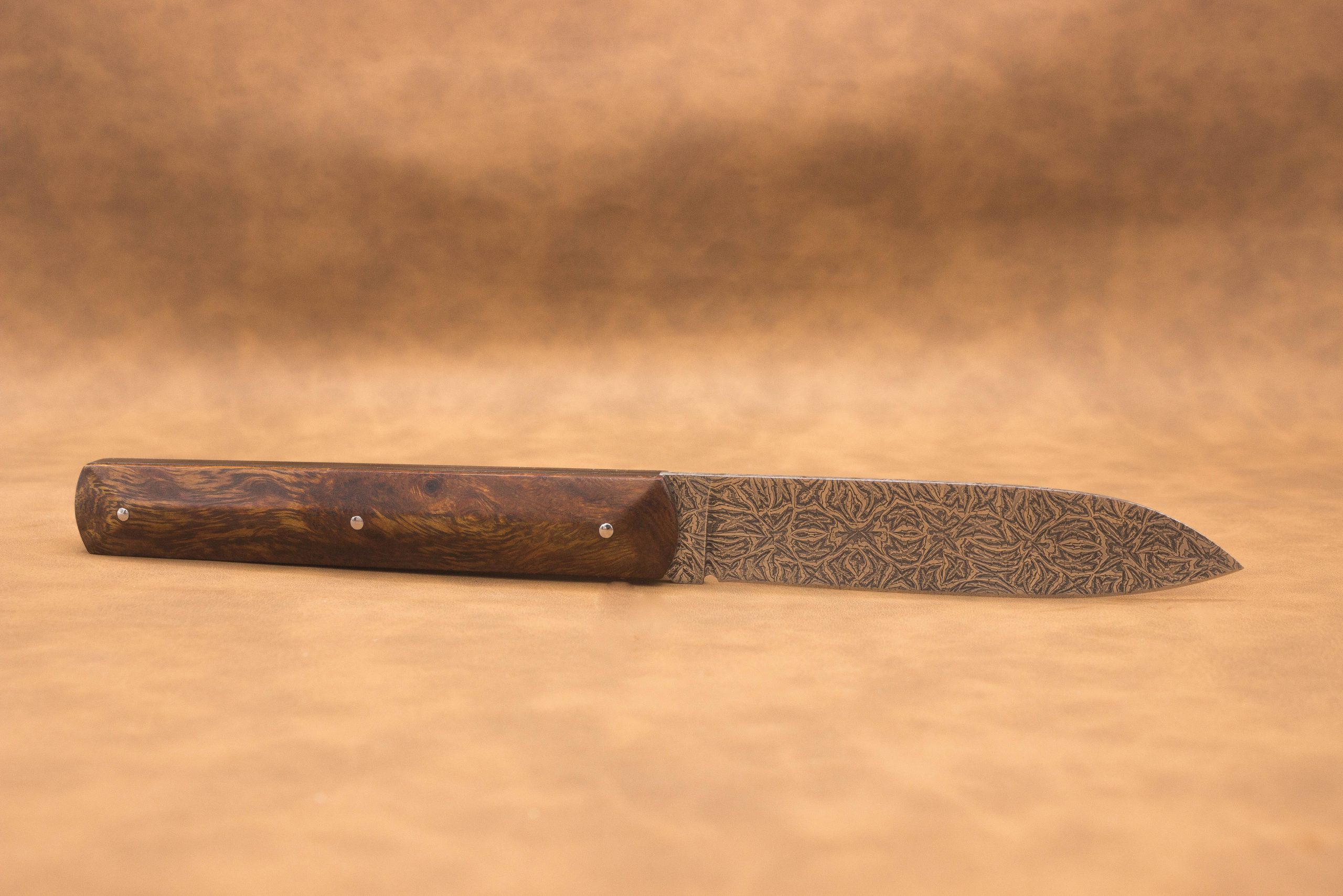 Vue générale : Couteau droit artisanal en damas mosaïque avec manche en bois de fer d'Arizona. Lame : Lame en damas carbone mosaïque forgée artisanalement. Manche : Manche en bois de fer d'Arizona sur couteau artisanal français. Dos : Dos poli d'un couteau à cran forcé fabriqué à la main. Étui : Étui en véritable cuir noir livré avec le couteau artisanal joel alexanian couteau d'art collection damas maison var